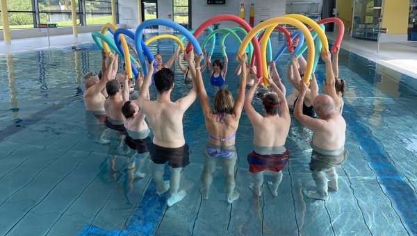 Eine Gruppe von Menschen stehen kreisförmig im Wasser und halten bunte Wasserschlangen in die Luft. 