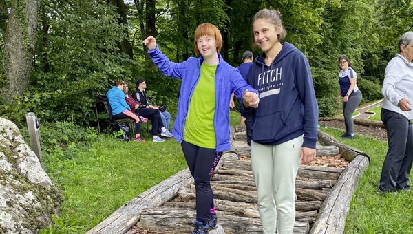 Zwei Frauen laufen Hand in Hand über einen Barfusspfad.