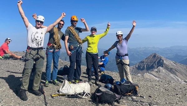 Eine Gruppe hat einen Berg erklommen und schaut glücklich in die Kamera.